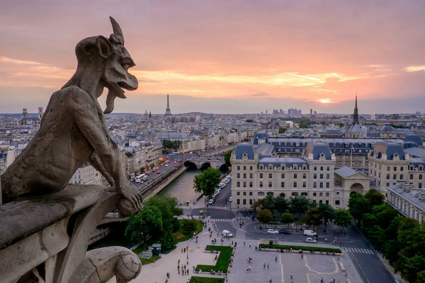 A stone gargoyle on Notre-Dame looking out over Paris and the Seine at sunset